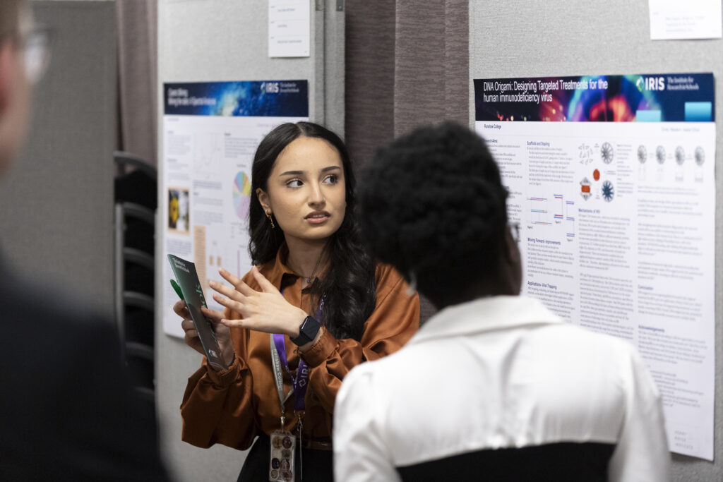 A female student presents her research findings next to her poster